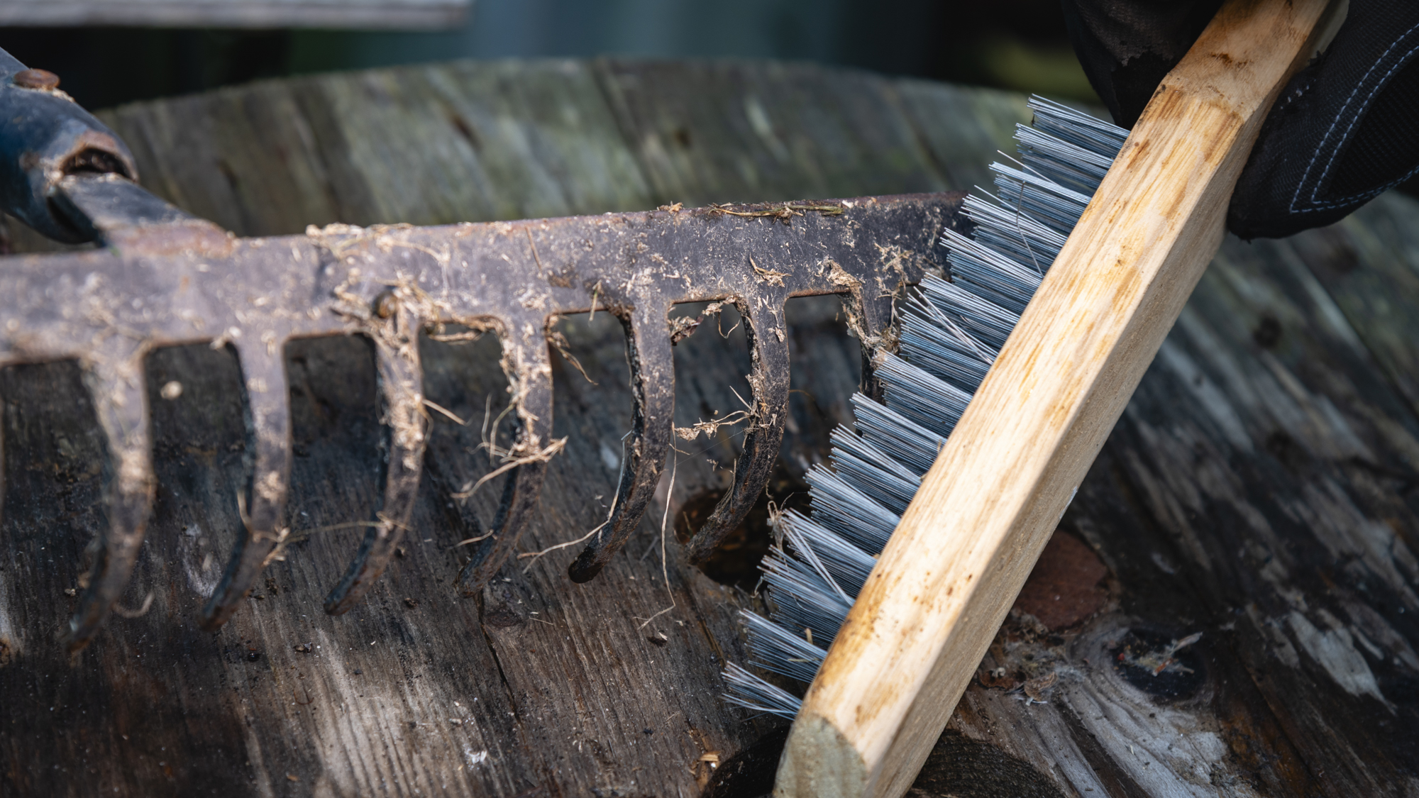 Borstar av jord från trädgårdsredskap på ett träbord i höstljus.